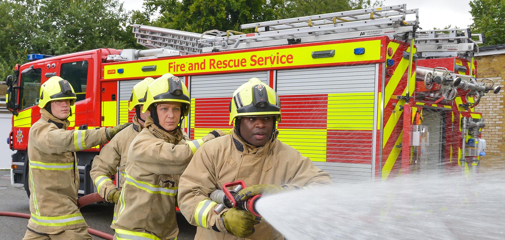 Four firefighters using hose by fire engine