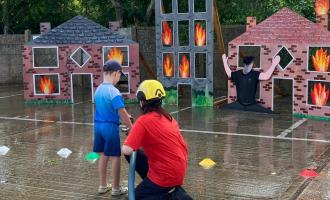 Adult and child with a hose pointing towards wooden building cut-outs