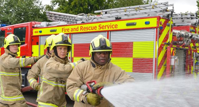 Four firefighters using hose by fire engine